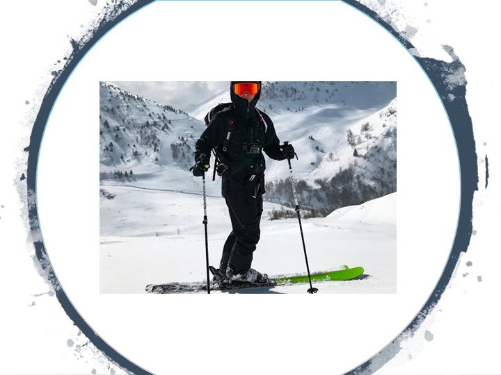 Un homme sur une montagne en hiver, debout sur une planche de ski, équipé de deux bâtons, de lunettes et d'une veste de ski.
